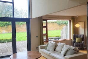 Uma sala de estar moderna com um sofá, uma mesa redonda e janelas amplas com vista para um jardim.