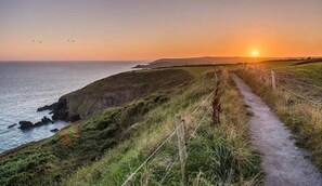 A coastal path with a fence, grassy terrain, and a sunset over the sea. - Luxury 2 Bed Lodge, Beside Castlemartyr Resort (Castlemartyr)