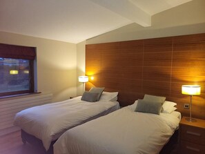 Habitación de hotel con dos camas, cabecero de madera, lámparas de noche y una ventana con cortinas.