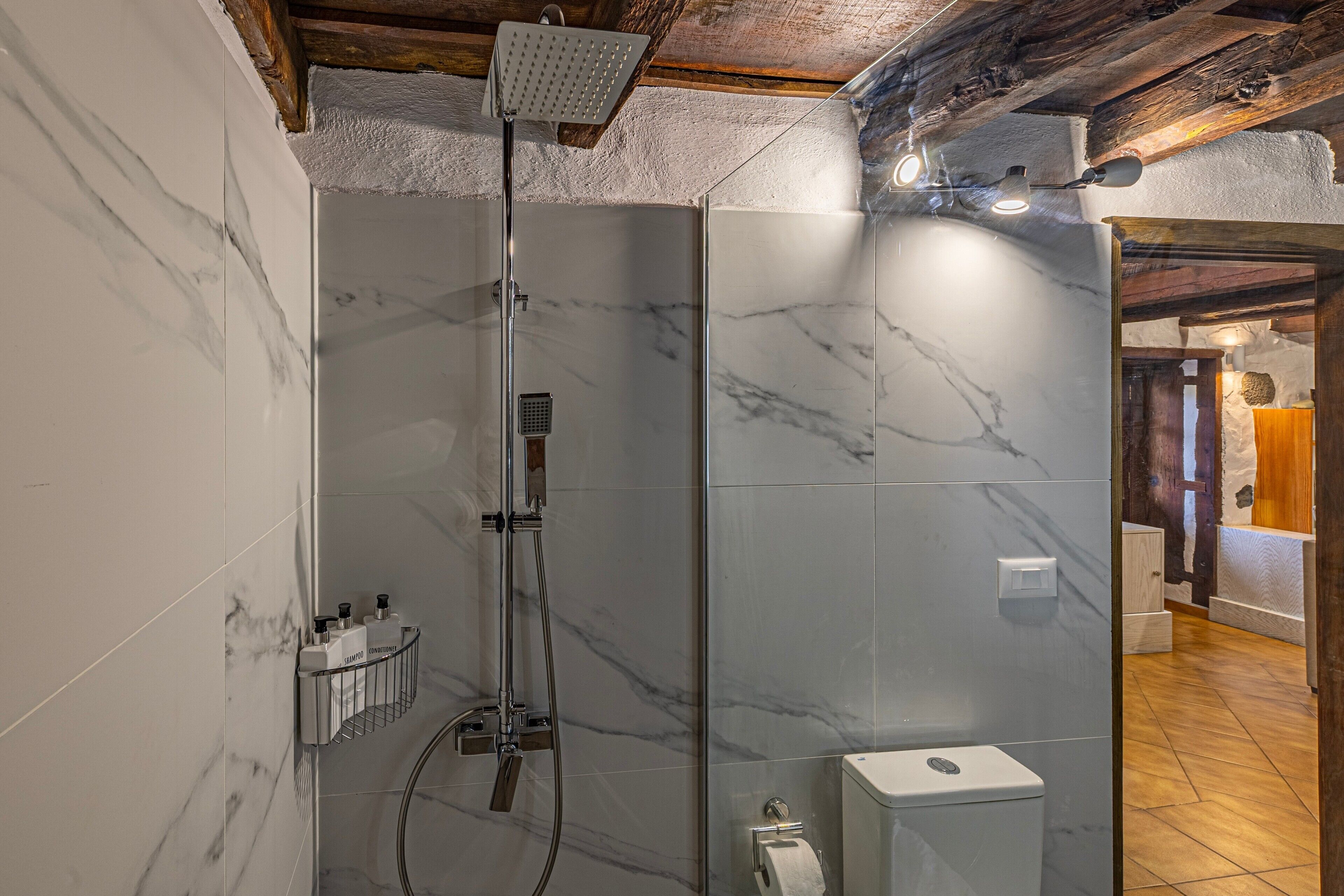 A modern bathroom with a glass-enclosed shower, marble walls, and a wooden ceiling.