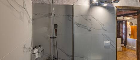 A modern bathroom with a glass-enclosed shower, marble walls, and a wooden ceiling.