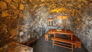 A stone-walled room with a wooden table and benches, a hanging light fixture, and a framed picture on the wall. - Casa Yuliana: Private Heated Pool and Sea Views (Tijarafe)