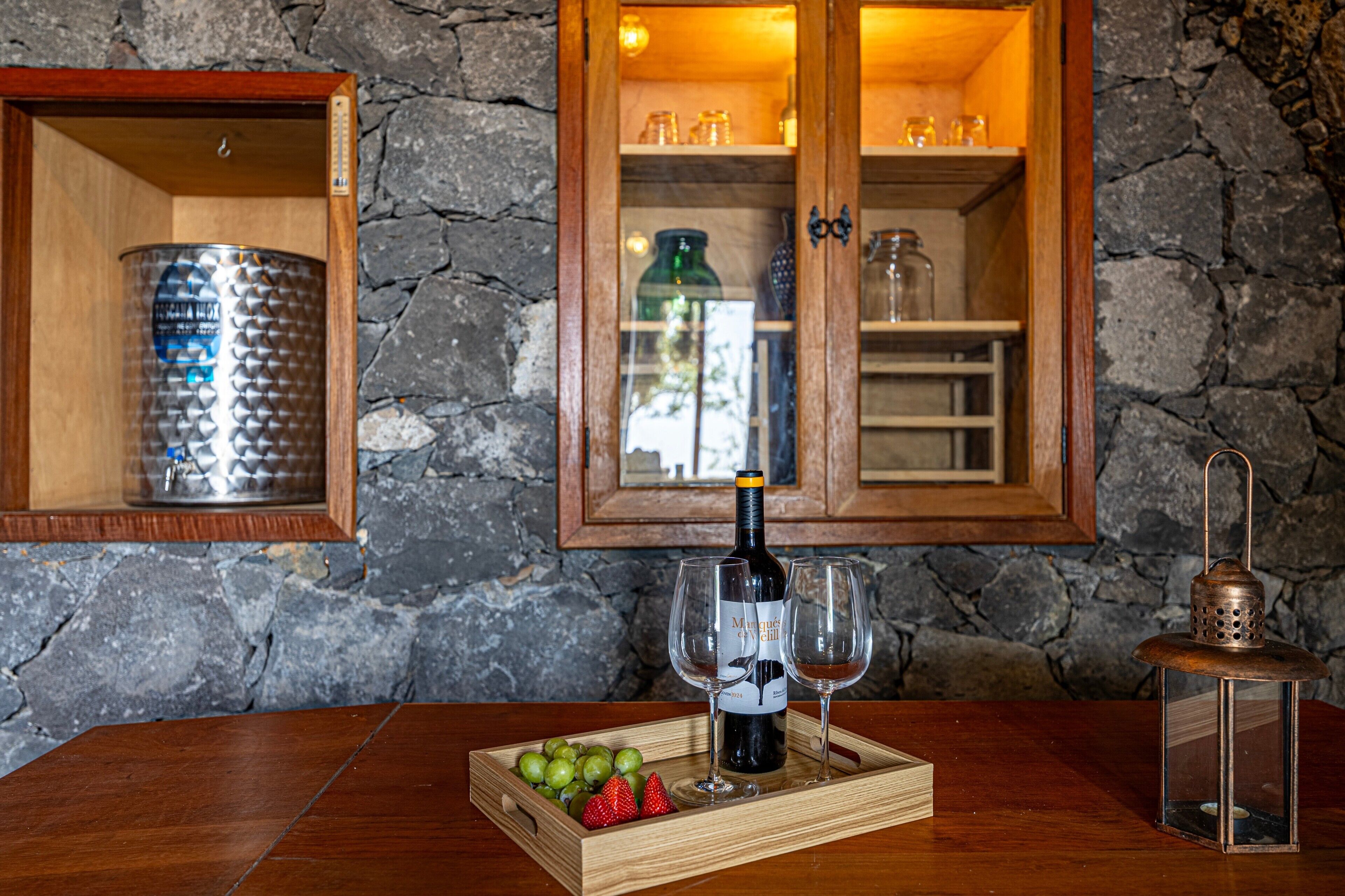 Une table en bois sur laquelle se trouvent une bouteille de vin, deux verres et une assiette de raisins et de fraises.