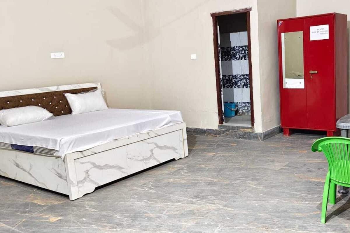 A room with a bed, a red cabinet, and green chairs around a table.