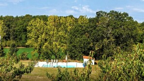 A rural landscape with a white building, a green field, and dense trees in the background. - GITE HIBISCUS (Sanilhac)
