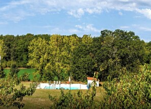 Ländliche Landschaft mit einem weißen Gebäude, einem grünen Feld und dichter Baumgruppe im Hintergrund.