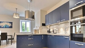 A modern kitchen with blue cabinets, stainless steel appliances, and a dining area with a table and chairs. - GITE HIBISCUS (Sanilhac)