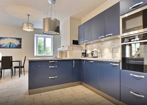 Eine moderne Küche mit blauen Schränken, Edelstahlgeräten und einem Essbereich mit Tisch und Stühlen.