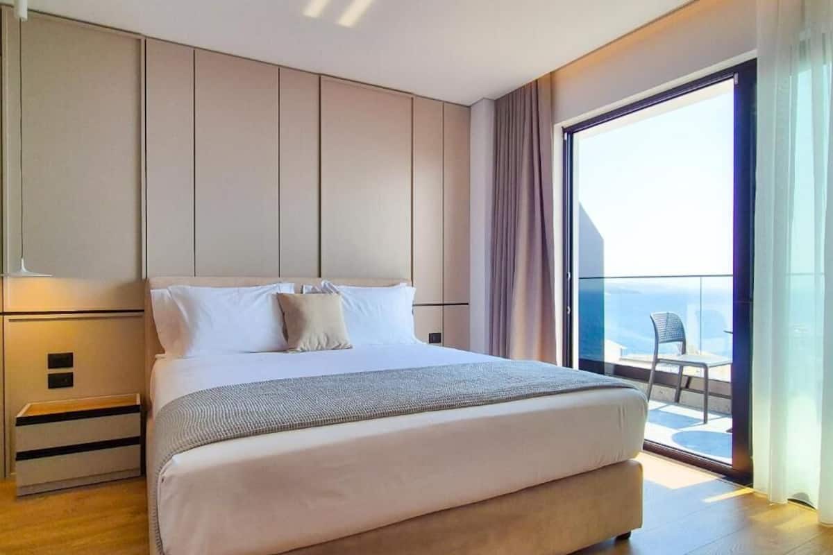 Quarto de hotel moderno com uma cama grande, uma mesa de cabeceira, uma janela com vista e uma varanda.