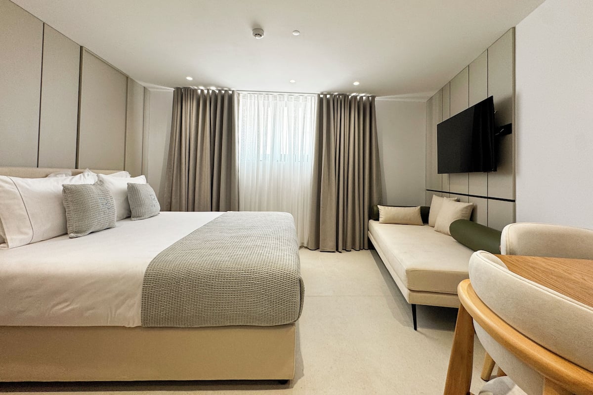 Quarto de hotel moderno com cama, sofá, televisão e janela com cortinas.