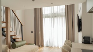 Ein modernes Wohnzimmer mit Treppe, einer Couch, einem Esstisch und einem an der Wand befestigten Fernseher.