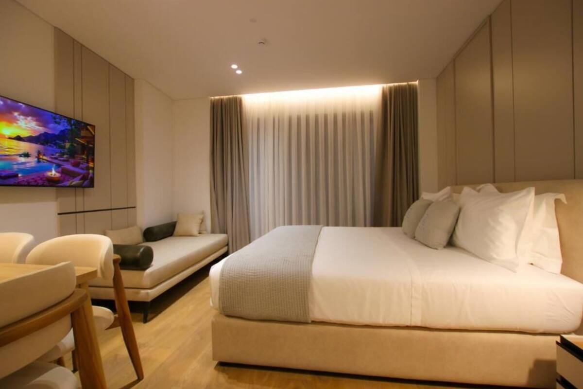 Quarto de hotel moderno com uma cama grande, televisão de tela plana, sofá e escrivaninha.