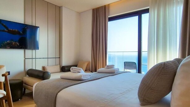 Ein modernes Hotelzimmer mit einem großen Bett, einem flachbildfernseher an der Wand, einem Balkon mit Vorhängen und Blick auf die Stadt.