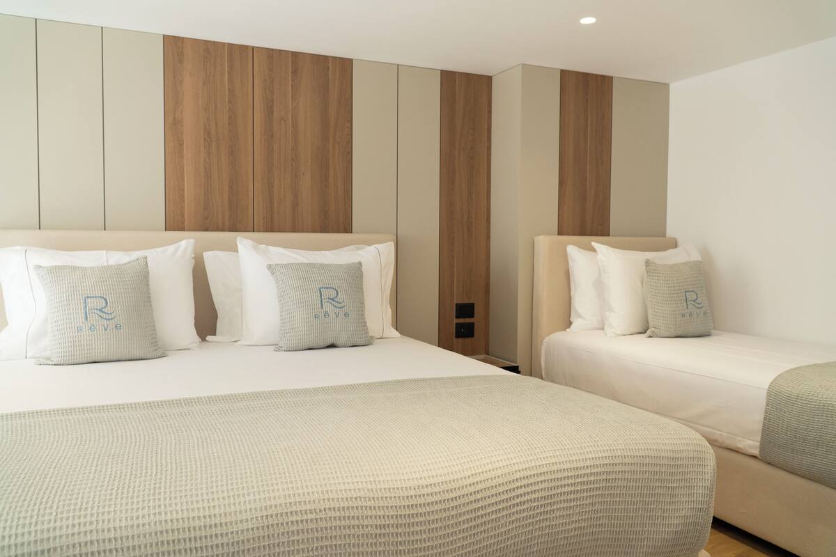 Quarto de hotel com duas camas, parede revestida de madeira e esquema de cores neutras.