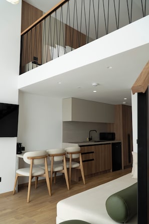 A modern kitchen with wooden cabinets, a dining area with a table and chairs, and a staircase with a railing. - Rêve Studio Apartments (Sarande)