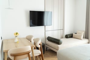A modern room with a wooden dining table, chairs, a sofa, and a flat-screen TV mounted on the wall. - Rêve Studio Apartments (Sarande)