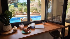 Ein Essbereich mit Blick auf einen Swimmingpool, einer Pflanze, einem Croissant und einer Tasse Kaffee auf einem Holztisch.