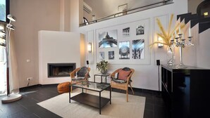 Ein modernes Wohnzimmer mit Kamin, zwei Korbsessel, einem Glastisch und einer schwarzen Konsole mit einem Kandelaber.