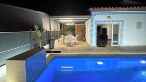 En swimmingpool med ett överbyggt område, en liten byggnad med kakelbeklädd fasad och en satellantenn.