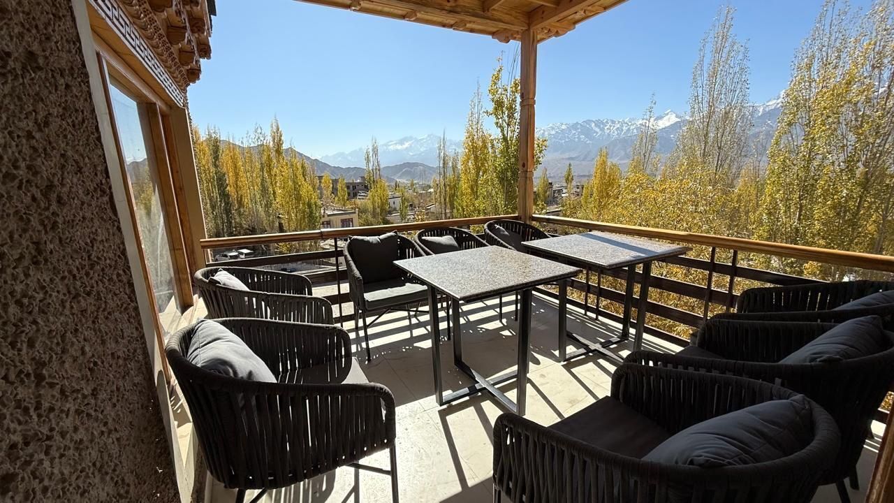 A covered outdoor seating area with tables and chairs, a view of mountains, and a wooden pergola.