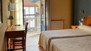 A room with a wooden ceiling, a bed, a table with a lamp, and a view through a door.