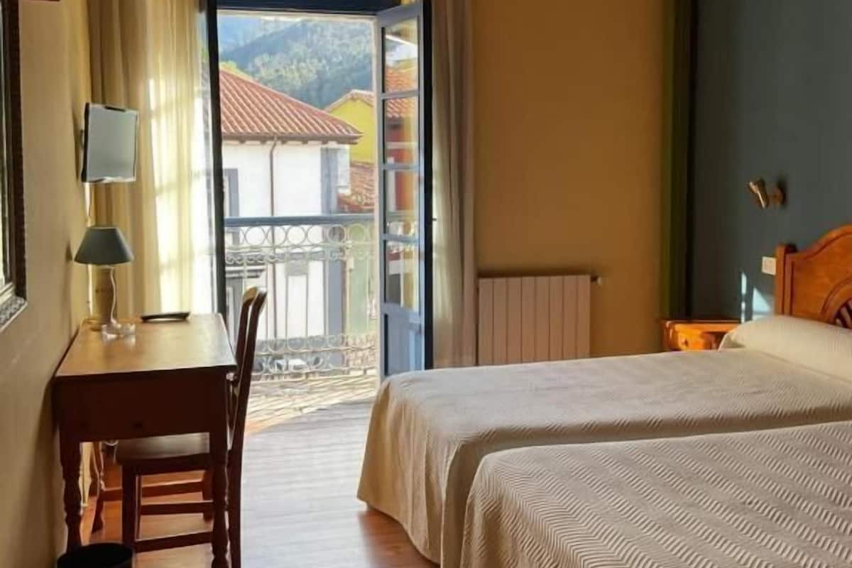 Une pièce avec un plafond en bois, un lit, une table avec une lampe et une vue sur l’extérieur, visible à travers une porte.