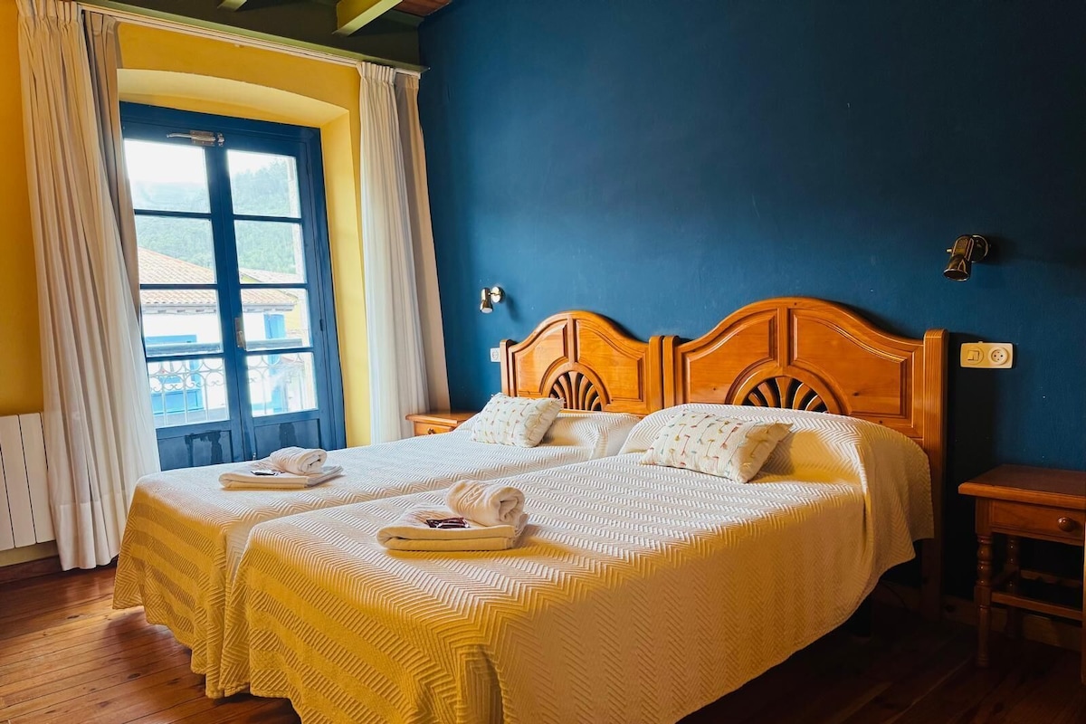 Cama doble con cabecera de madera, dos almohadas y una toalla doblada a cada lado.