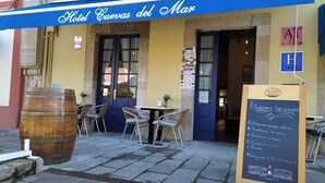 A hotel entrance with a blue awning, outdoor seating, a large wooden barrel, and a chalkboard sign listing breakfast items. - HOTEL CUEVAS DEL MAR (Nueva)