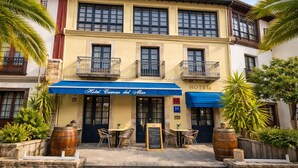 A hotel with a blue awning, outdoor seating, and palm trees.