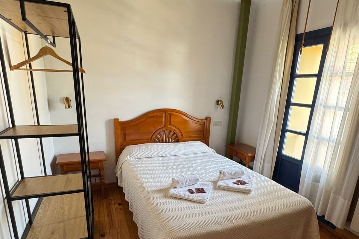 Une chambre à coucher avec un lit en bois, une étagère en métal, une table de chevet en bois et une fenêtre avec des rideaux.