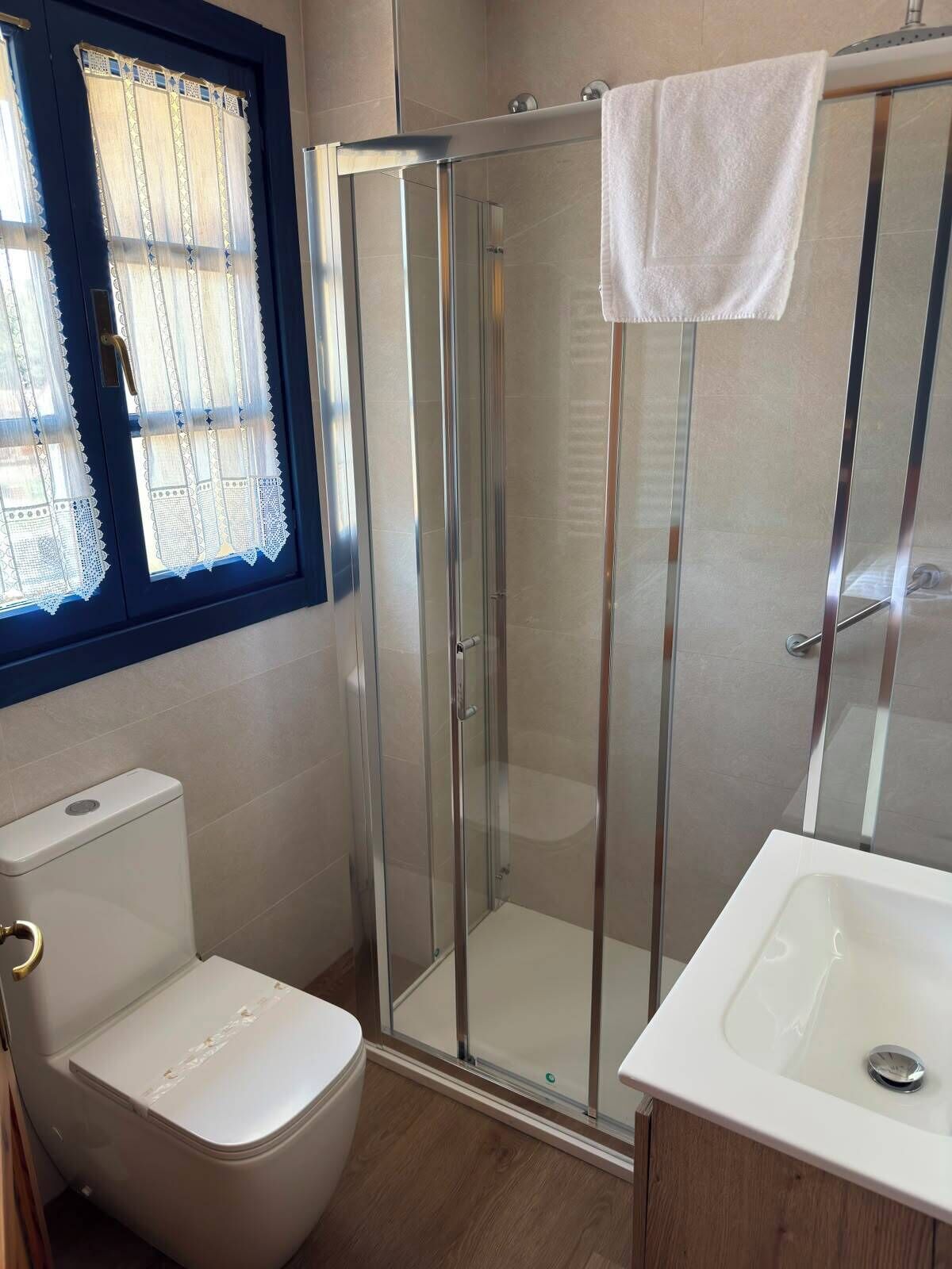 Un baño con ducha envuelta en vidrio, inodoro y lavamanos.