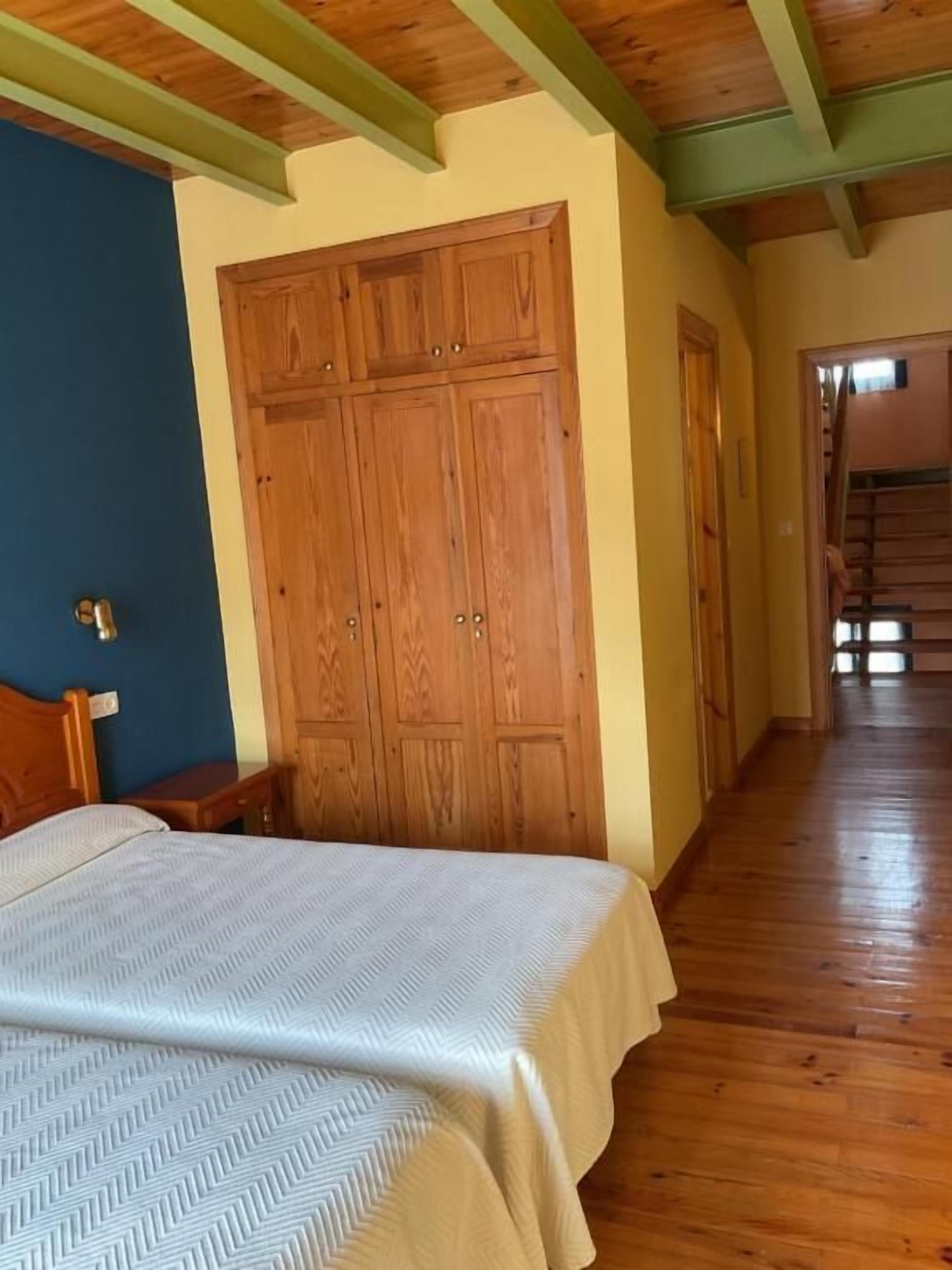 A bedroom with a bed, wooden wardrobe, and a hallway leading to a staircase.