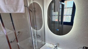 A modern bathroom with a glass-enclosed shower, a white sink, and a round mirror.