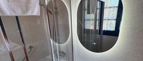 Un baño moderno con ducha envuelta en vidrio, un lavabo blanco y un espejo redondo.