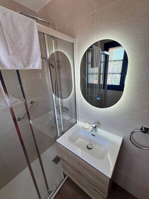 A modern bathroom with a glass-enclosed shower, a white sink, and a round mirror. - HOTEL CUEVAS DEL MAR (Nueva)