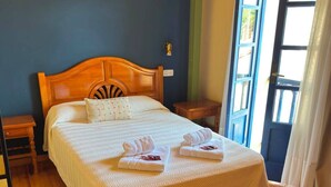 A neatly made bed with a wooden headboard, a bedside table, and a view of the outdoors through a door. - HOTEL CUEVAS DEL MAR (Nueva)