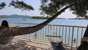 Un balcon avec un hamac, une vue sur la mer et un voilier à l’horizon.