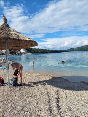 A beach with a thatched umbrella, pebbled shore, and calm water. - House Kala N29 (house with 3 bedrooms, max 6+2 persons, pet friendly) (Jezera)