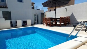 Une piscine avec une table et des chaises, une échelle et un bâtiment doté d’un toit en tuiles.