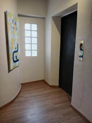 A hallway with a wooden floor, a black door, a window, and a wall-mounted elevator control panel. - Eastique Hotel Koh Chang (Ko Chang)