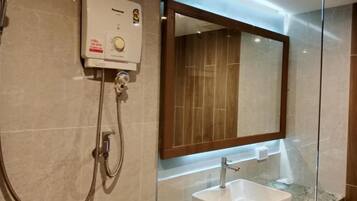 A bathroom with a glass enclosure, a built-in sink, a handheld showerhead, and a wall-mounted mirror.