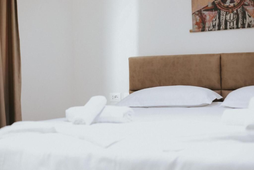 A neatly made bed with white linens and pillows, a brown headboard, and a wall-mounted painting.