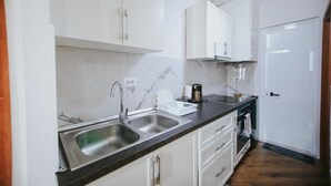 A kitchen with white cabinets, a marble backsplash, stainless steel sinks, and a black countertop. - Villa Reve de Tirana (Tirana)