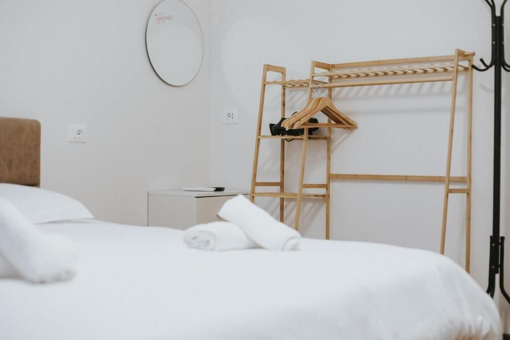 Una habitación de hotel con una cama, un perchero de madera, una mesita de noche pequeña y un espejo en la pared.