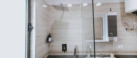 A modern bathroom with a glass shower enclosure, a white sink, and a marble-tiled wall.
