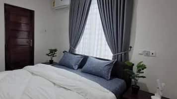 Un dormitorio con cama, mesita de noche, planta en maceta y ventana con cortinas.
