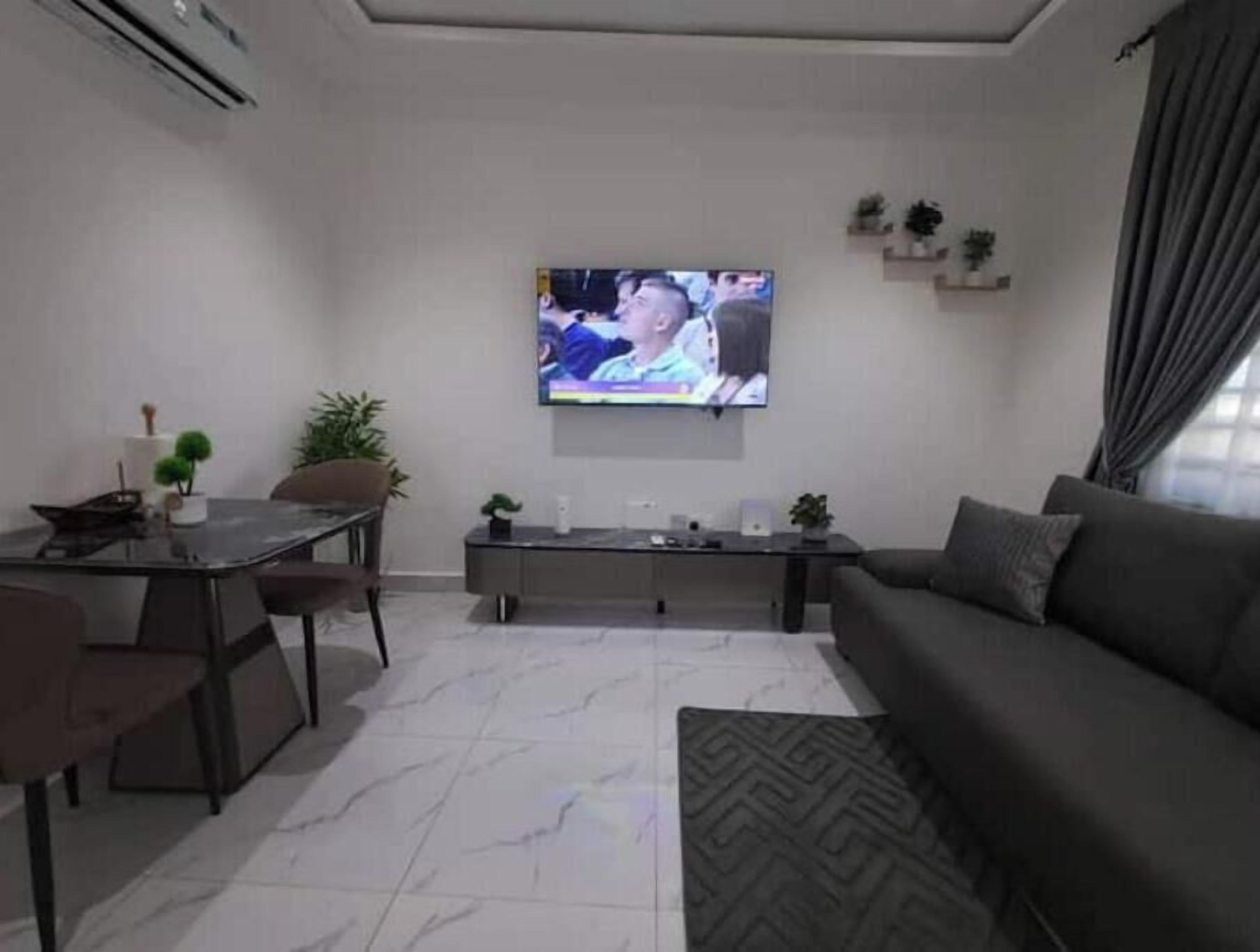 A modern living room with a flat-screen TV, a dining table, chairs, a sofa, and a coffee table.