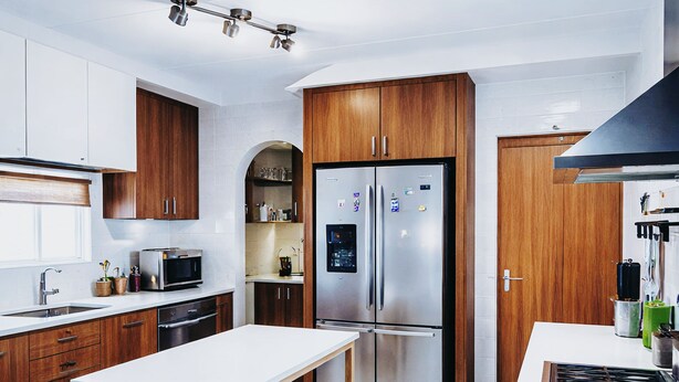 Una cocina moderna con armarios de madera, un refrigerador de acero inoxidable, una encimera blanca y un horno empotrado.
