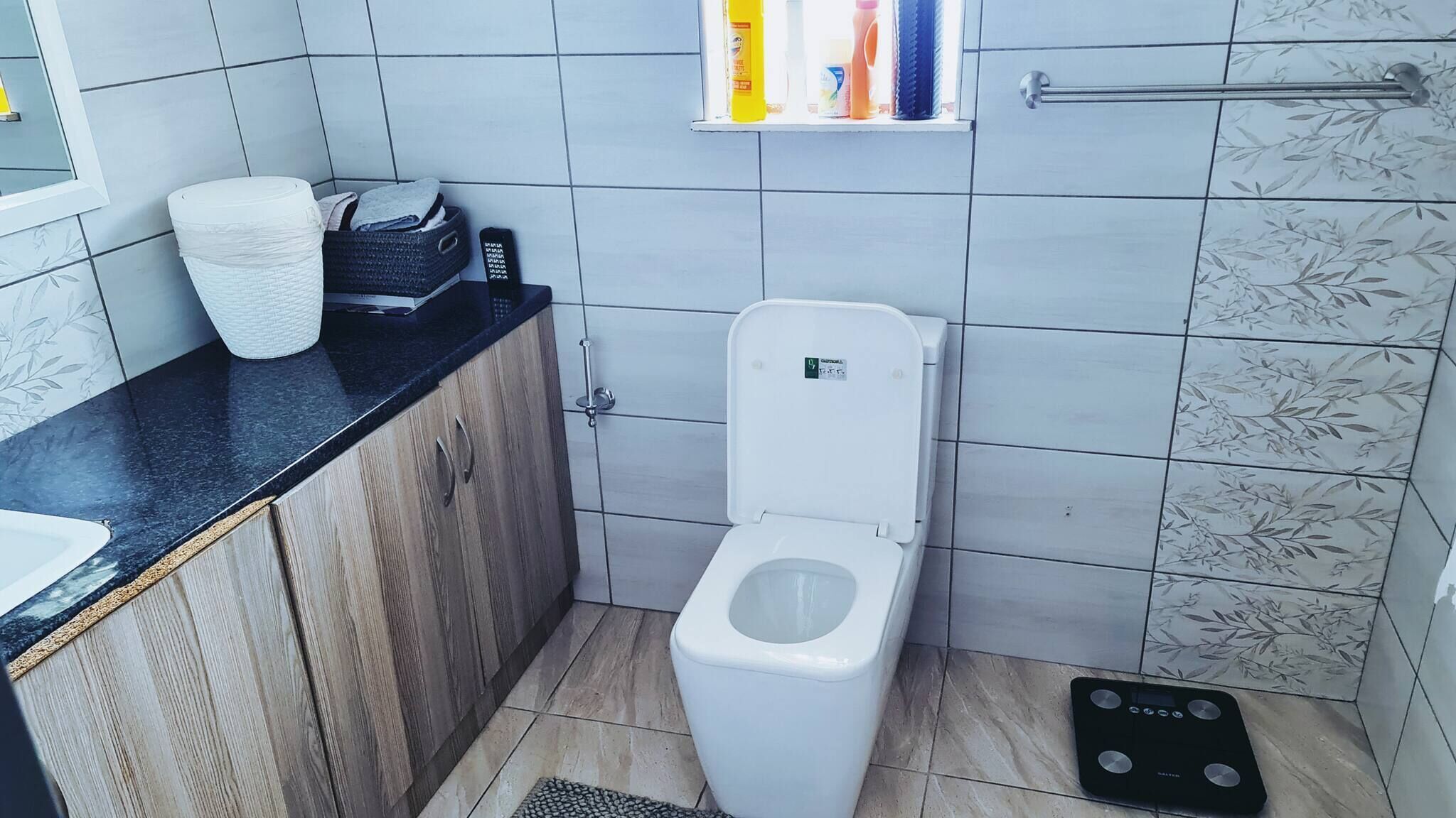 Un baño con inodoro, lavamanos, zona de ducha y un estante pequeño con artículos de aseo.