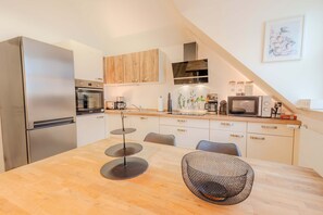 Una cocina moderna con un refrigerador de acero inoxidable, armarios de madera, una mesa de comedor con sillas y un microondas.